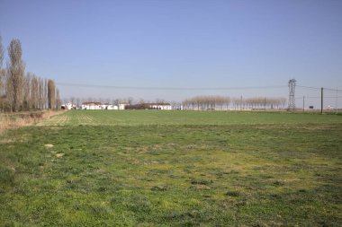 Yanı başında ağaçlar ve ufukta İtalya kırsalında bir köşk olan boş bir çayır.