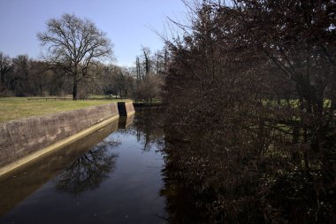 Kırsal kesimdeki bir parktaki bir şatonun hendeğinde gökyüzü ve suya dökülen ağaçlar.