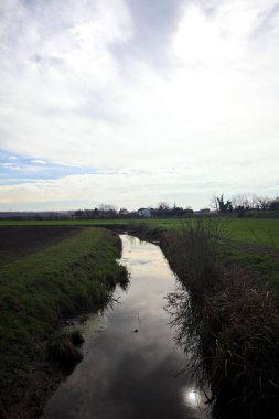 Güneş tarafından aydınlatılan kısmen bulutlu bir günde gökle ekili tarlalar arasındaki hendek.