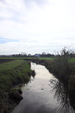 Güneş tarafından aydınlatılan kısmen bulutlu bir günde gökle ekili tarlalar arasındaki hendek.