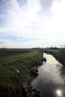 Güneş tarafından aydınlatılan kısmen bulutlu bir günde gökle ekili tarlalar arasındaki hendek.