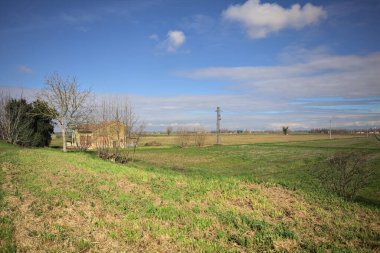 Güneşli bir günde ufka kadar uzanan bir tarladaki kır evi bir setten görülüyor.