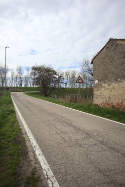 Bulutlu bir günde, bir köyün köy yolu bir evin yanındaki setin üzerine tırmanıyor.