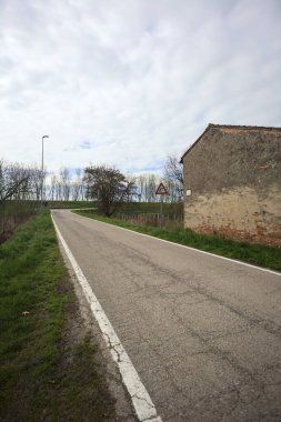 Bulutlu bir günde, bir köyün köy yolu bir evin yanındaki setin üzerine tırmanıyor.