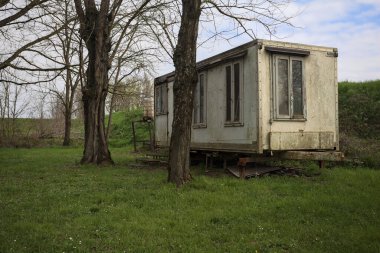 Terk edilmiş prefabrik edilmiş bir bina İtalya kırsalında çıplak ağaçlarla çevrili bir çimenlikte.