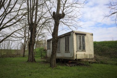 Terk edilmiş prefabrik edilmiş bir bina İtalya kırsalında çıplak ağaçlarla çevrili bir çimenlikte.
