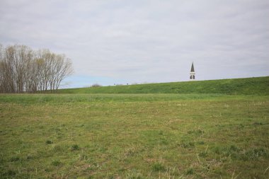 Bulutlu bir günde, İtalya 'nın kırsal kesimindeki bir toprak setinin arkasında çan kulesi olan çan tarlası rüzgârla süpürüldü.