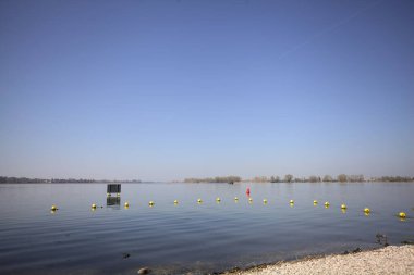 Şamandıralarla çevrili çakıl taşlı göl kıyıları ve güneşli bir günde suya atılmış bir tabela.