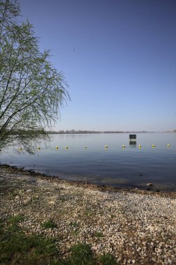 Şamandıralarla çevrili çakıl taşlı göl kıyıları ve güneşli bir günde suya atılmış bir tabela.