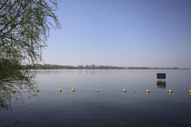 Şamandıralarla çevrili çakıl taşlı göl kıyıları ve güneşli bir günde suya atılmış bir tabela.
