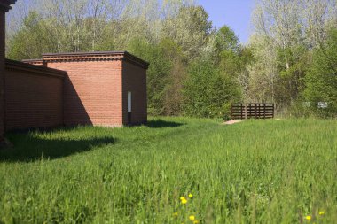 Çimenlikteki tuğla yapı ve güneşli bir günde parkın çimlerini çevreleyen hendeğin üzerindeki ahşap köprü.