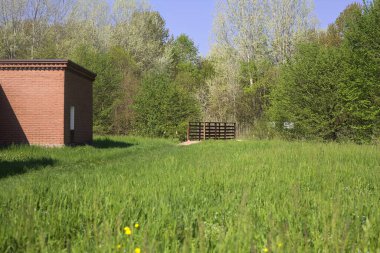 Çimenlikteki tuğla yapı ve güneşli bir günde parkın çimlerini çevreleyen hendeğin üzerindeki ahşap köprü.