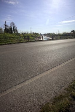 İtalya 'nın kırsal kesimindeki bir köprü tarafından çerçevelenen koruluklar arasında beton bir nehir yatağında oyalama kanalı.