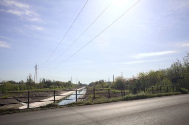 İtalya 'nın kırsal kesimindeki bir köprü tarafından çerçevelenen koruluklar arasında beton bir nehir yatağında oyalama kanalı.