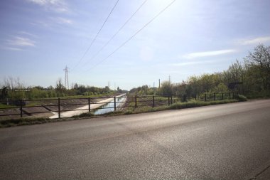 İtalya 'nın kırsal kesimindeki bir köprü tarafından çerçevelenen koruluklar arasında beton bir nehir yatağında oyalama kanalı.