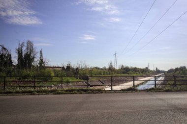 İtalya 'nın kırsal kesimindeki bir köprü tarafından çerçevelenen koruluklar arasında beton bir nehir yatağında oyalama kanalı.