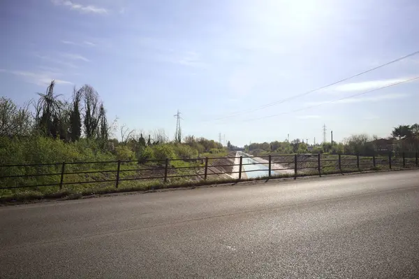 İtalya 'nın kırsal kesimindeki bir köprü tarafından çerçevelenen koruluklar arasında beton bir nehir yatağında oyalama kanalı.