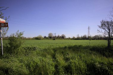 Ağaçlarla çevrili güneşli bir günde, üzerinde koruluğu olan bir toprak seti ile çevrili bir elektrik hattıyla ekilmiş alan.