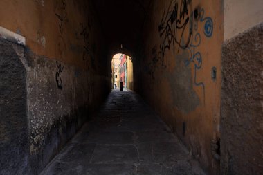 Duvarlarında grafiti olan dar bir sokak ve karşı ucunda da bir sütun var.