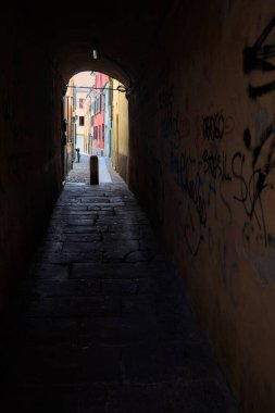 Duvarlarında grafiti olan dar bir sokak ve karşı ucunda da bir sütun var.