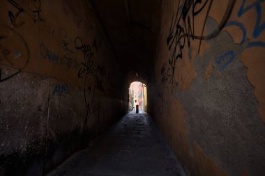 Duvarlarında grafiti olan dar bir sokak ve karşı ucunda da bir sütun var.