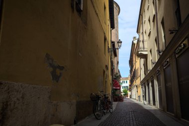 Bir İtalyan kasabasında güneşli bir günde, uzaktaki bir meydanda sona eren gölgede dar bir sokak.