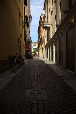 Bir İtalyan kasabasında güneşli bir günde, uzaktaki bir meydanda sona eren gölgede dar bir sokak.