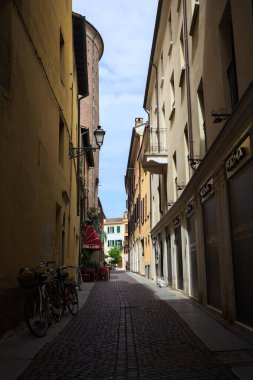 Bir İtalyan kasabasında güneşli bir günde, uzaktaki bir meydanda sona eren gölgede dar bir sokak.