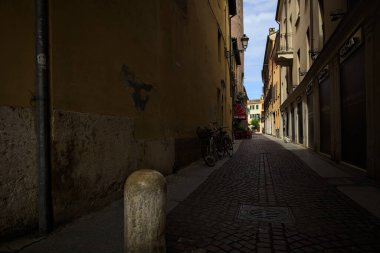 Bir İtalyan kasabasında güneşli bir günde, uzaktaki bir meydanda sona eren gölgede dar bir sokak.