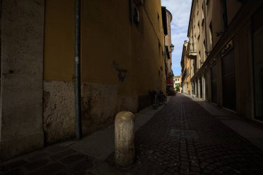 Bir İtalyan kasabasında güneşli bir günde, uzaktaki bir meydanda sona eren gölgede dar bir sokak.