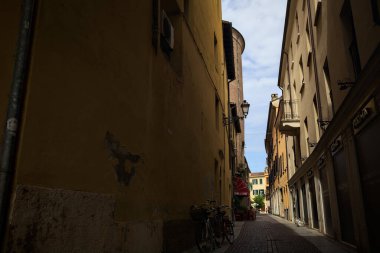 Bir İtalyan kasabasında güneşli bir günde, uzaktaki bir meydanda sona eren gölgede dar bir sokak.