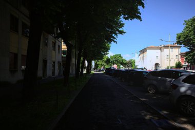 Mantova, İtalya - 25 Nisan 2025 - İtalya 'nın bir şehrinde, yerde uzun gölgeler bırakan ağaçların yanında bir bulvar ve park yeri