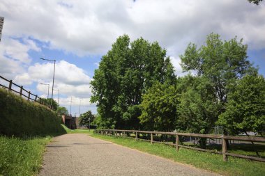 Ağaçlarla çevrili bir çimenliğin kenarındaki yol ve güneşli bir günde bir parktaki set arasında.