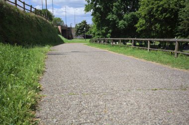 Ağaçlarla çevrili bir çimenliğin kenarındaki yol ve güneşli bir günde bir parktaki set arasında.
