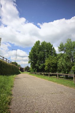 Ağaçlarla çevrili bir çimenliğin kenarındaki yol ve güneşli bir günde bir parktaki set arasında.