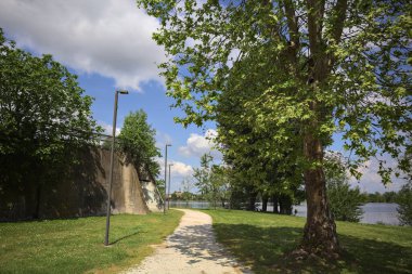 Güneşli bir günde, gölün kıyısındaki beton set ve ağaçlar arasındaki toprak izi.
