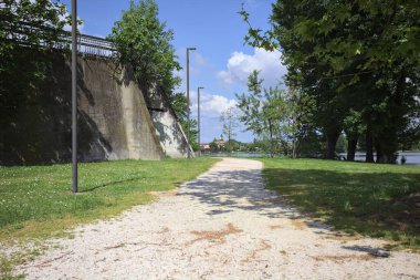 Güneşli bir günde, gölün kıyısındaki beton set ve ağaçlar arasındaki toprak izi.
