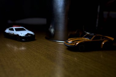 Mantova, İtalya - 29. Nisan 2025 - 1 / 64 Hot Wheels ve Takara Tomi kopyaları turuncu Nissan Fairlady Z ve Nissan Fairlady Z Nismo Japon polis arabası teneke bir oyuncak tencerenin yanında yol bariyeri simülasyonu yapıyor