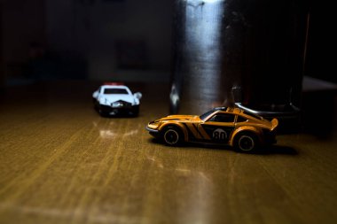 Mantova, İtalya - 29. Nisan 2025 - 1 / 64 Hot Wheels ve Takara Tomi kopyaları turuncu Nissan Fairlady Z ve Nissan Fairlady Z Nismo Japon polis arabası teneke bir oyuncak tencerenin yanında yol bariyeri simülasyonu yapıyor