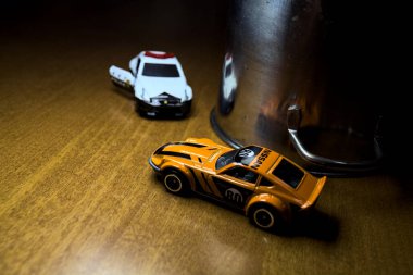 Mantova, İtalya - 29. Nisan 2025 - 1 / 64 Hot Wheels ve Takara Tomi kopyaları turuncu Nissan Fairlady Z ve Nissan Fairlady Z Nismo Japon polis arabası teneke bir oyuncak tencerenin yanında yol bariyeri simülasyonu yapıyor