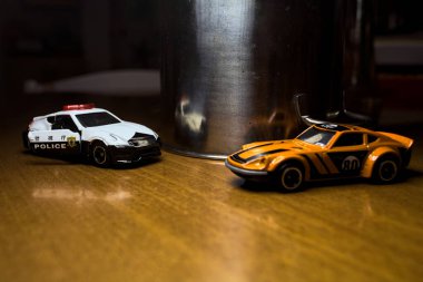 Mantova, İtalya - 29. Nisan 2025 - 1 / 64 Hot Wheels ve Takara Tomi kopyaları turuncu Nissan Fairlady Z ve Nissan Fairlady Z Nismo Japon polis arabası teneke bir oyuncak tencerenin yanında yol bariyeri simülasyonu yapıyor