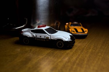 Mantova, İtalya - 29. Nisan 2025 - 1 / 64 Hot Wheels ve Takara Tomi kopyaları turuncu Nissan Fairlady Z ve Nissan Fairlady Z Nismo Japon polis arabası teneke bir oyuncak tencerenin yanında yol bariyeri simülasyonu yapıyor