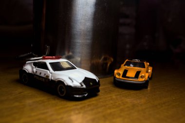 Mantova, İtalya - 29. Nisan 2025 - 1 / 64 Hot Wheels ve Takara Tomi kopyaları turuncu Nissan Fairlady Z ve Nissan Fairlady Z Nismo Japon polis arabası teneke bir oyuncak tencerenin yanında yol bariyeri simülasyonu yapıyor