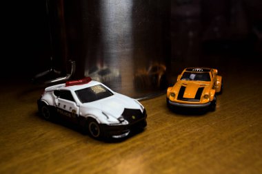 Mantova, İtalya - 29. Nisan 2025 - 1 / 64 Hot Wheels ve Takara Tomi kopyaları turuncu Nissan Fairlady Z ve Nissan Fairlady Z Nismo Japon polis arabası teneke bir oyuncak tencerenin yanında yol bariyeri simülasyonu yapıyor