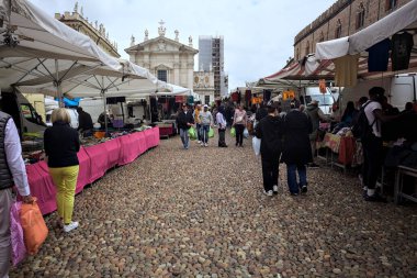 Mantova, İtalya - 8. Mart 2025 - Arka planda bir kilise olan bir sarayın ve insanların market tezgahlarına göz attığı bir meydanın yanındaki kaldırımlı meydan