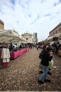 Mantova, İtalya - 8. Mart 2025 - Arka planda bir kilise olan bir sarayın ve insanların market tezgahlarına göz attığı bir meydanın yanındaki kaldırımlı meydan