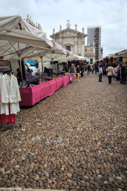 Mantova, İtalya - 8. Mart 2025 - Arka planda bir kilise olan bir sarayın ve insanların market tezgahlarına göz attığı bir meydanın yanındaki kaldırımlı meydan