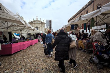 Mantova, İtalya - 8. Mart 2025 - Arka planda bir kilise olan bir sarayın ve insanların market tezgahlarına göz attığı bir meydanın yanındaki kaldırımlı meydan