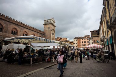Mantova, İtalya - 8. Mart 2025 - Pazar tezgahları ve bulutlu bir günde gezinen insanlarla çevrili bir sarayın yanından geçen cadde