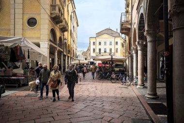 Mantova, İtalya - 8 Mart 2025 - Pazar tezgahları ve bulutlu bir günde kafelerin yanından geçen insanlar